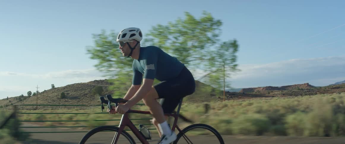 A cyclist pedals hard while riding a bicycle along a road through the countryside during the day