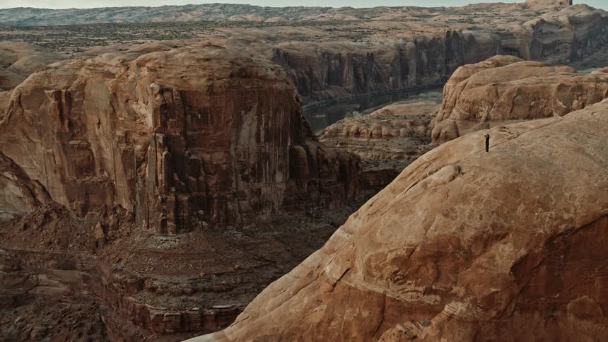A hiker stands on top of a massive canyon and looks at the view