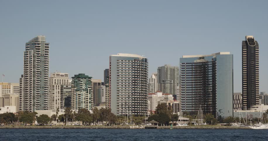 Sailboats sit in the lake next to the city buildings under a blue sky