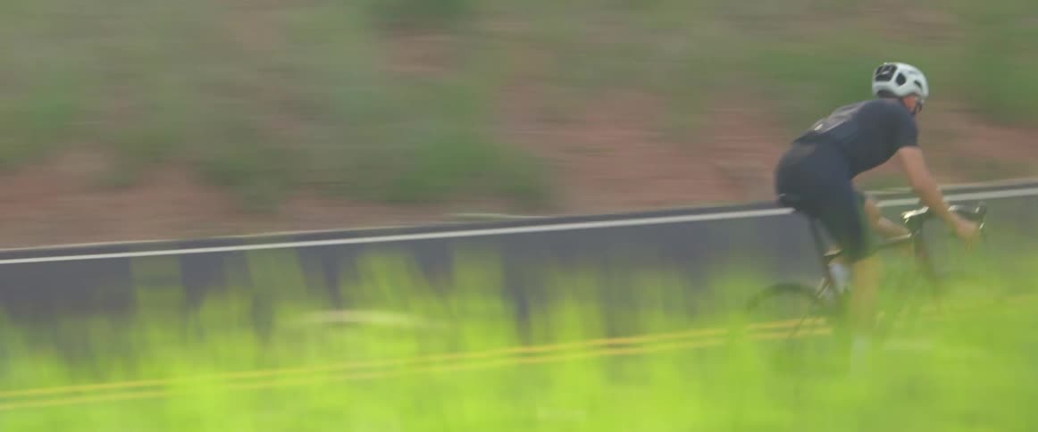 A man wearing a white helmet is riding a bicycle on a winding road through a forest