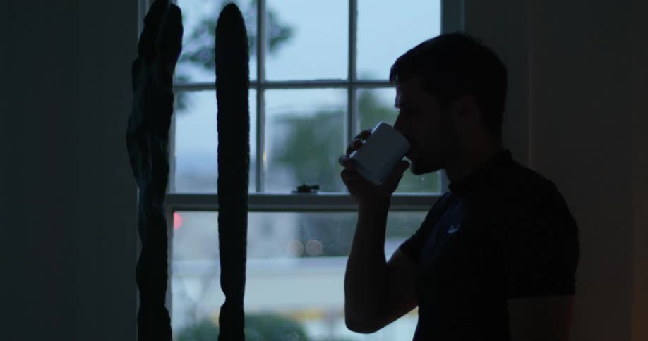 A man watches a storm from his window while drinking coffee