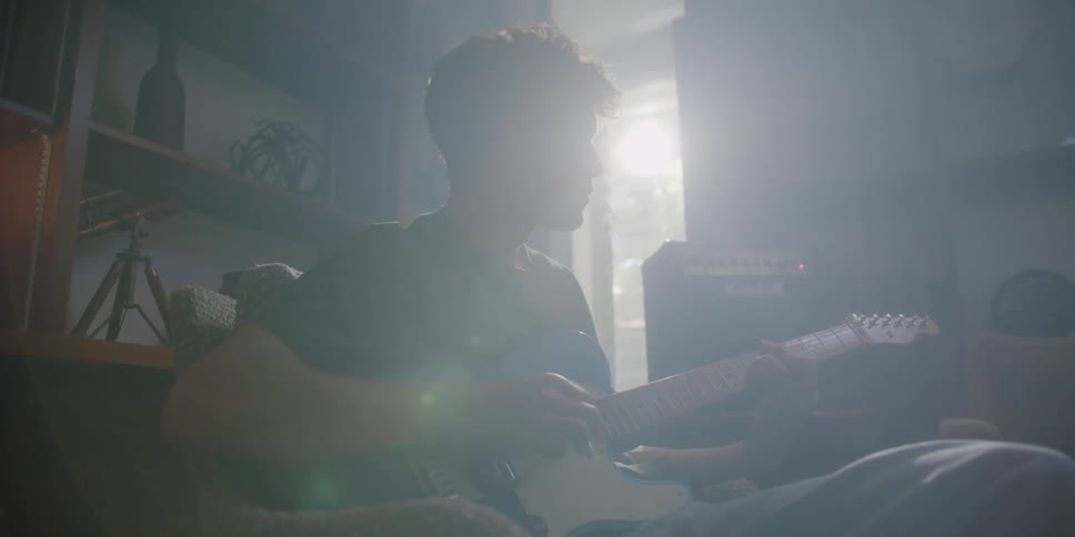 A man plays the guitar while sitting in a chair indoors during the day