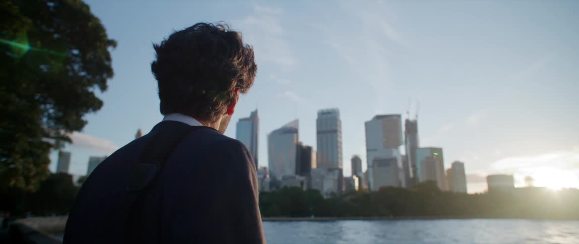 A man is standing on the shore of a lake looking across the water at a city skyline