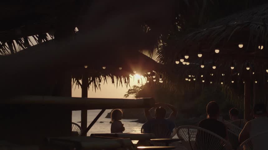 People are in a tropical setting on the water sitting at tables