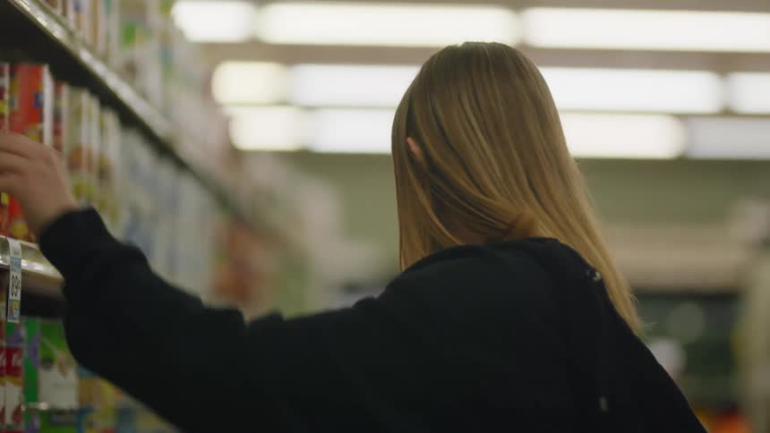 A young woman with ear buds in her ears is listening to music as she stocks the shelves in a grocery store