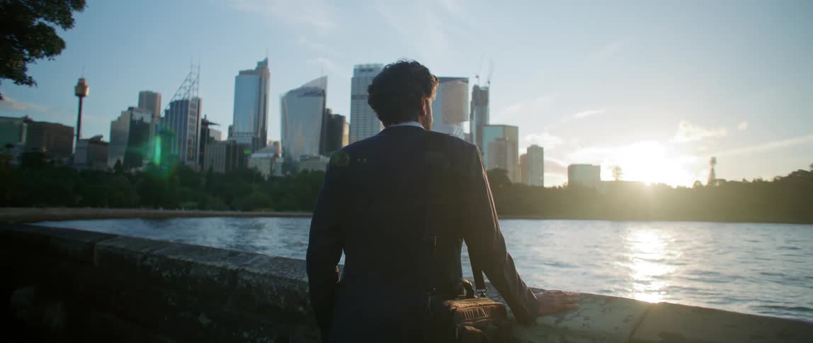 A man in a suit standing by a wall looking out over the water at the city skyline