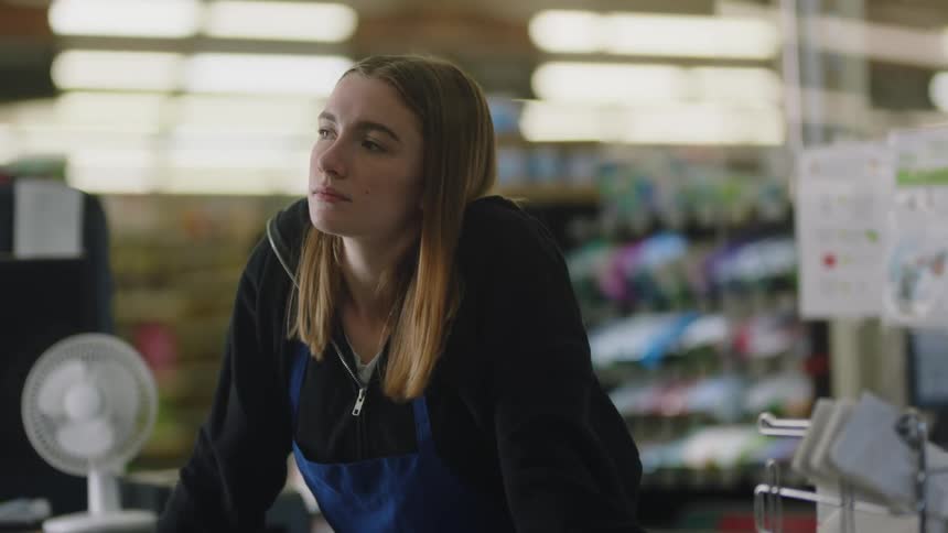 A cashier standing at her station in a store looking bored