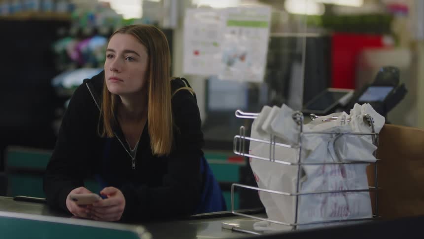A cashier leaning against the counter playing on her phone waiting for a customer