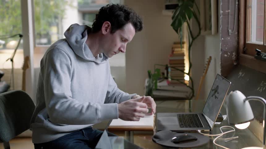 A man sitting down with a book at a computer