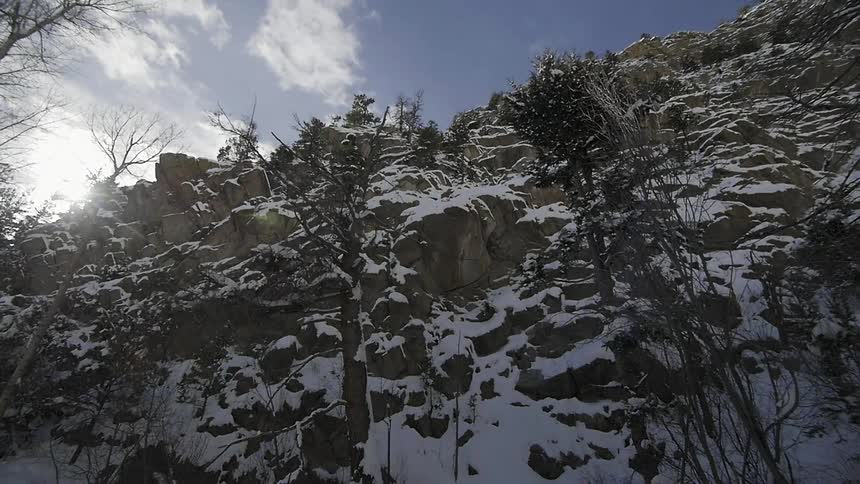 Looking from the ground to the top of a steep, rocky hillside covered with snow