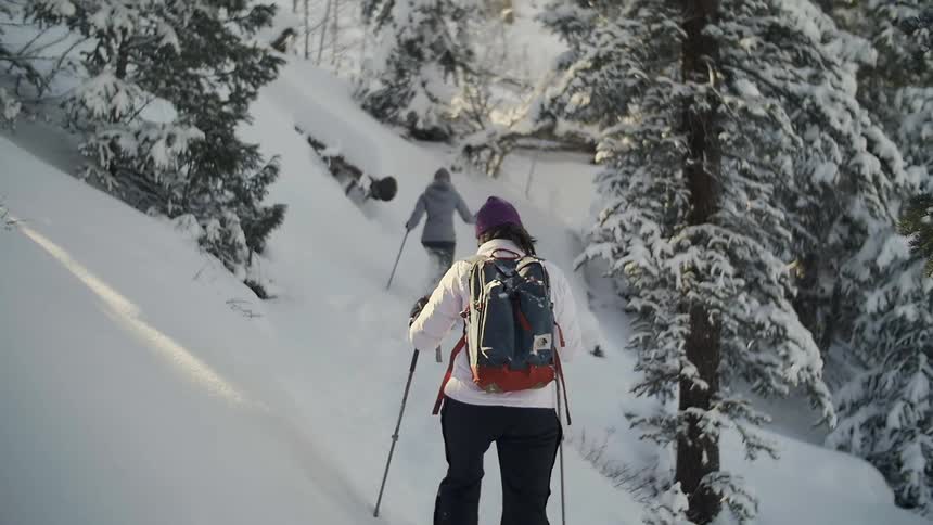 Two people are moving through deep snow on a hill with snow boots