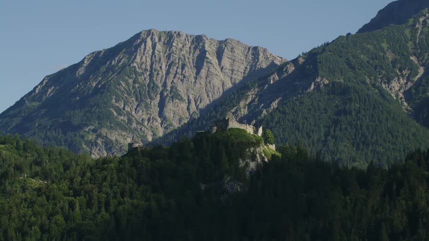 A dilapidated castle on atop a mountain ridge covered in thick forest during the day