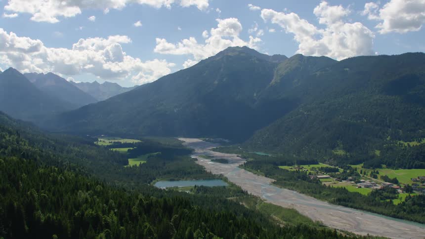 Aerial view of sunlight coming through the clouds over a field close to a river in the mountains