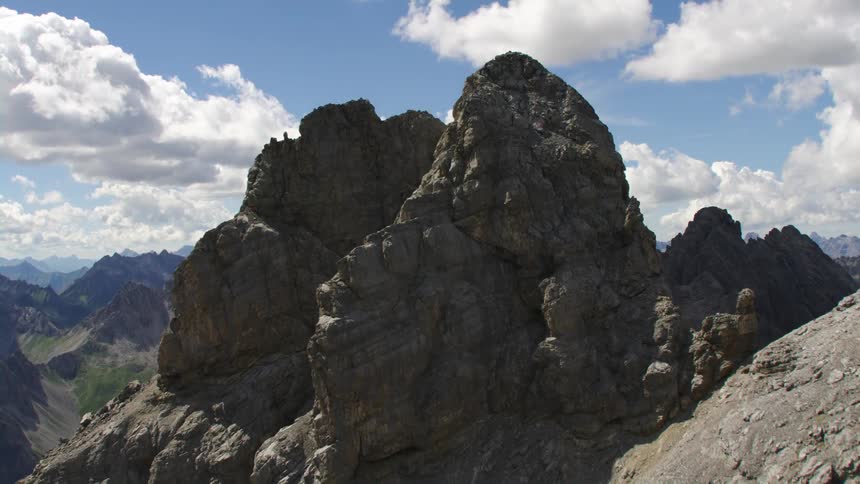Cross stands on craggy peak overlooking valley containing a lake in a mountain range