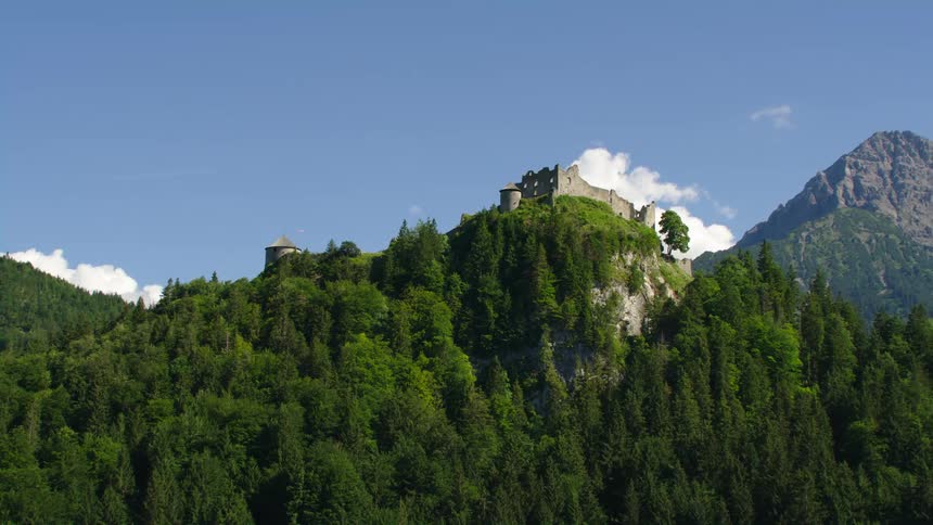 Ruins of large castle sit on mountain peak surrounded by forest