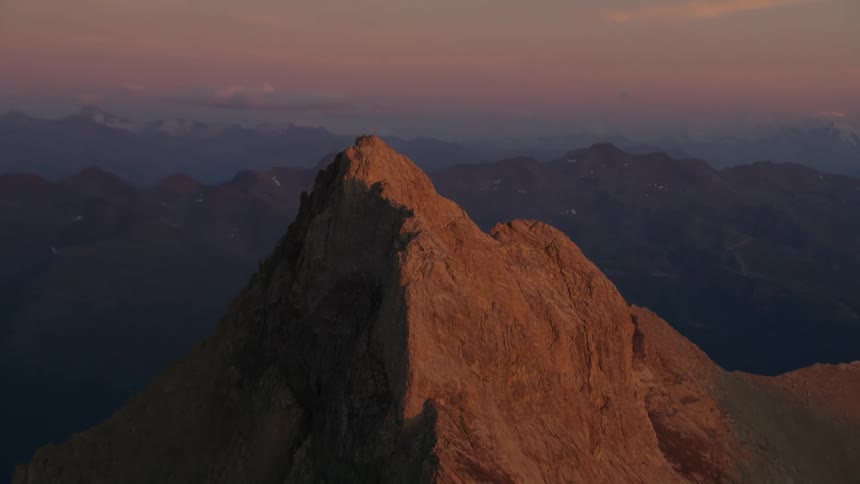 A cross on a mountain ridge in sunlight with a full moon in the sky on the horizon