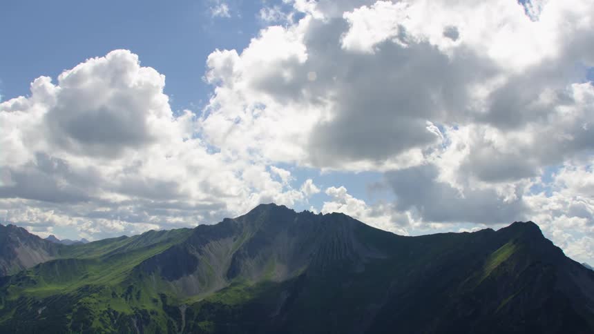 White clouds in a bright blue sky over green mountain ridges