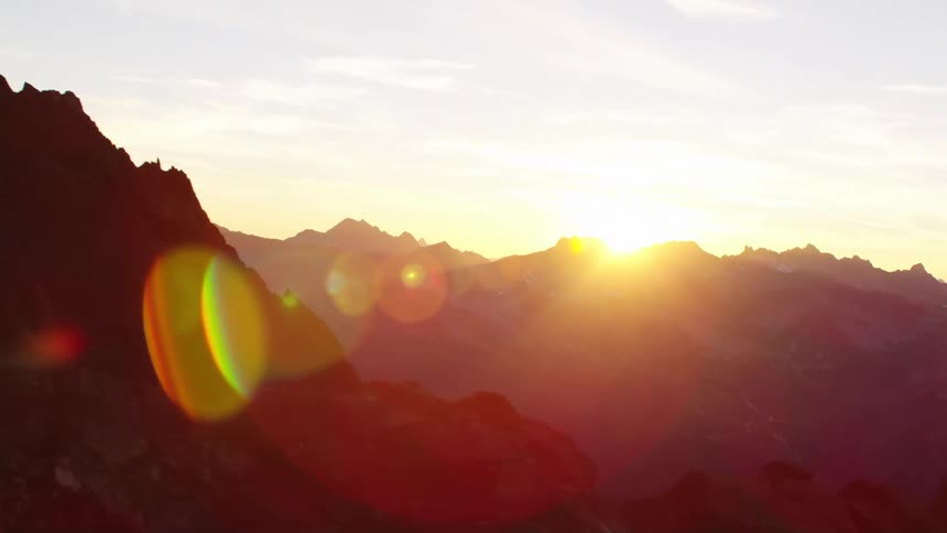 The sun shines brightly over a mountain ridge and there are mountains on the horizon