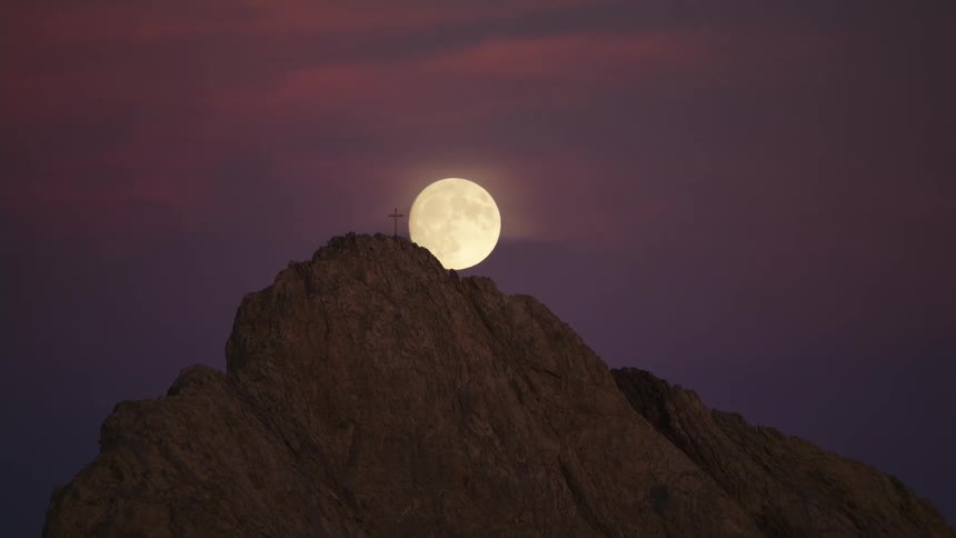 A full moon over a cliff with a cross