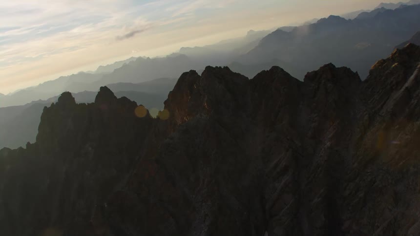 Twisting aerial footage of the silhouettes of the ridge of a mountain range at morning