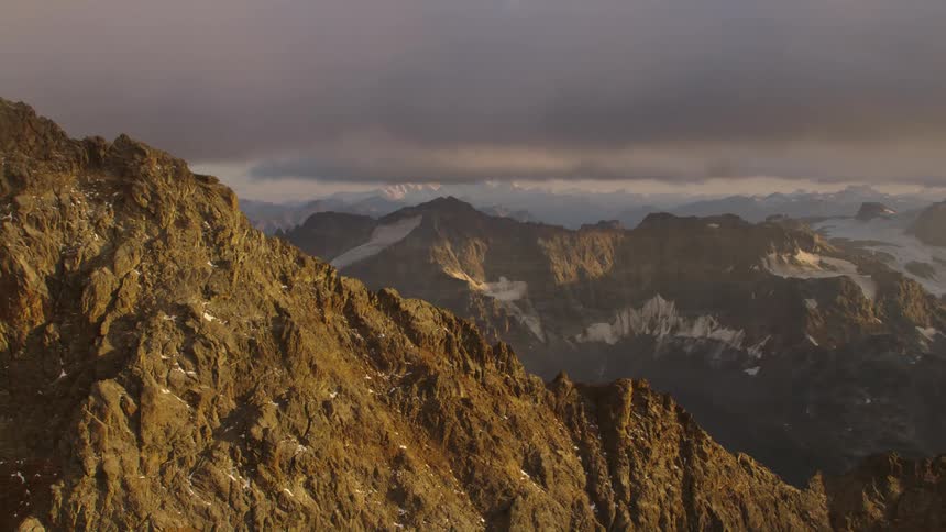 Aerial view of the rugged slopes of a mountain range under the clouds at evening
