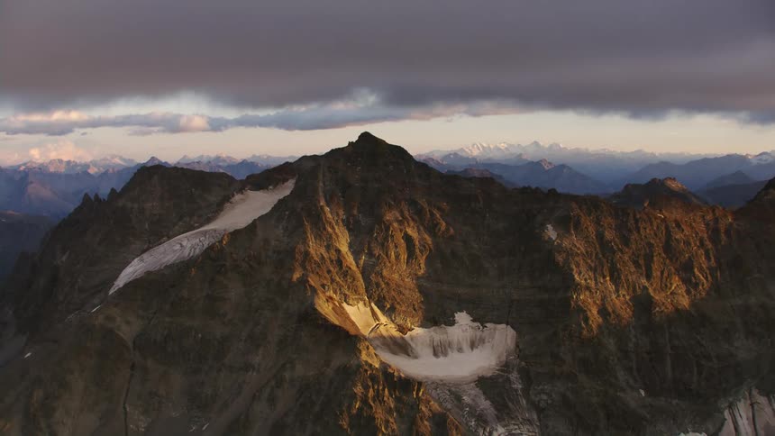 Mountain range with a frozen lake and peaks high in a cloudy sky and there are mountains in the distance