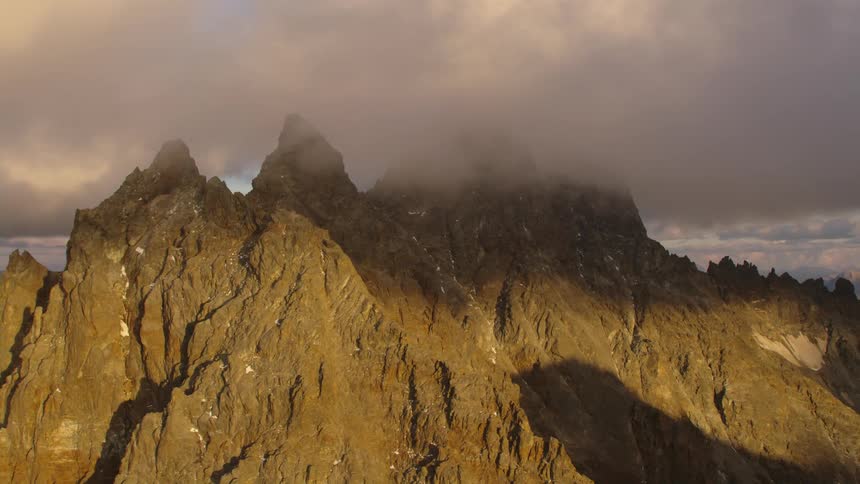 The sun shines on a mountain ridge with peaks high in the clouds