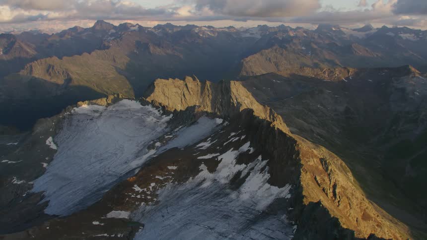 A mountain range covered in patches of snow in the evening