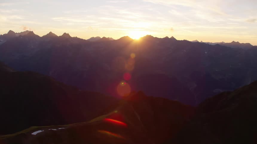 Aerial view of sunlight flaring over a mountain range at sunset