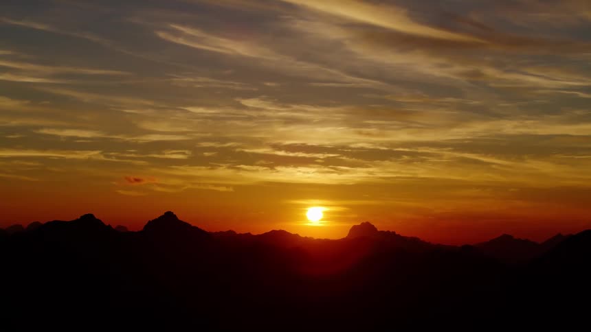 The sun sits low in the sky above the silhouette of a mountain range