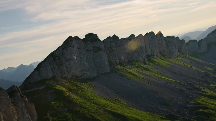 Rocky peaks on a mountain range reach high in a cloudy sky and there are mountains on the horizon