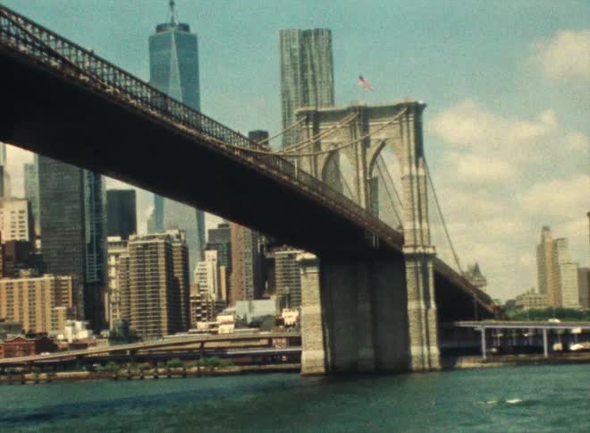A bridge over a waterway leading in to a city and cars driving on streets