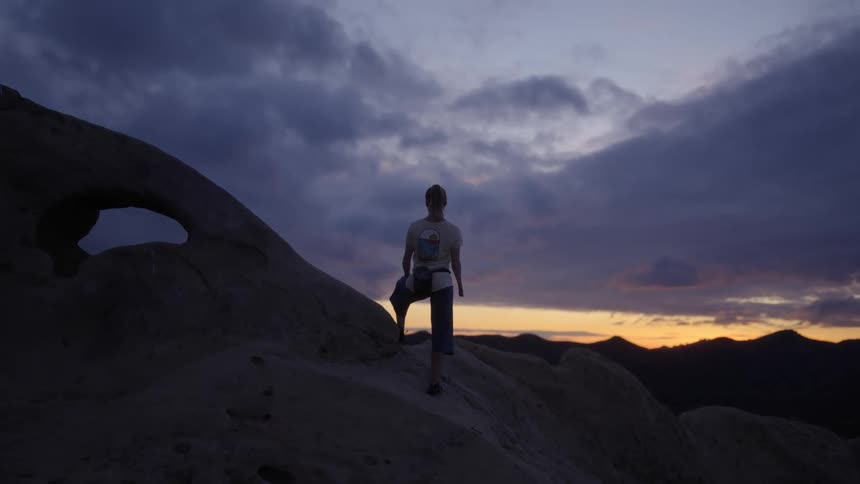 Woman stands on rock slope silhouetted against afterglow