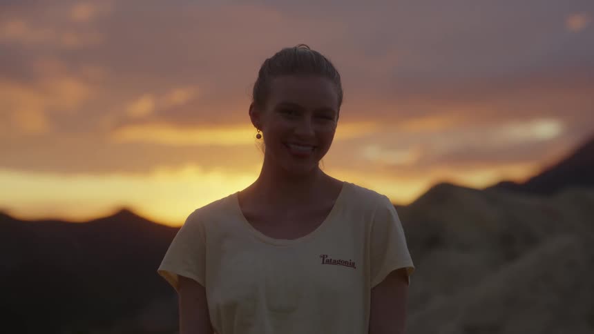 Woman stands outdoor smiling under a red sky with mountains in the background