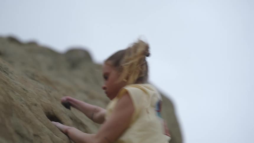 Blonde woman with a pony tail climbs up the rocks on a windy day