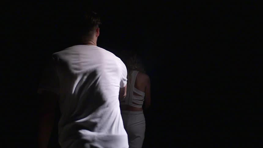 A man and woman holding hands while walking through a dark room