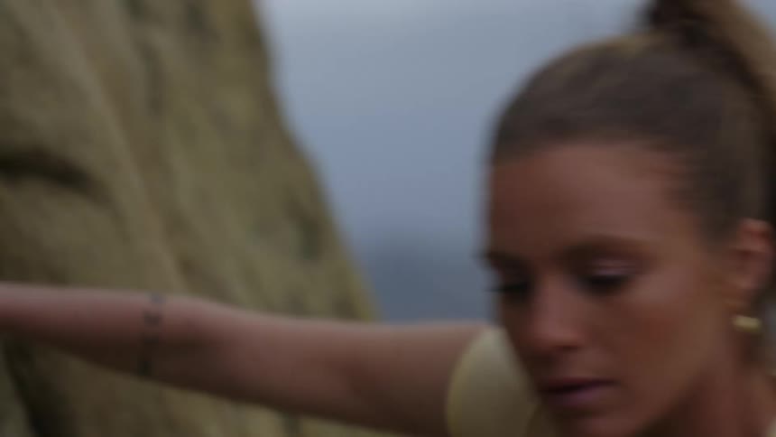 A woman is climbing the side of a mountain and she looks down as she pulls herself up