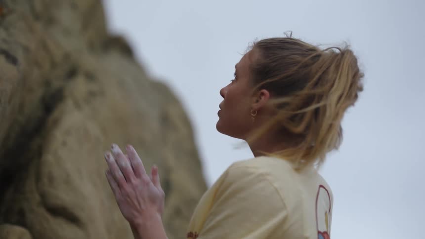 A woman rock climber rubs chalk on her hands looking up at the rock preparing for her climb