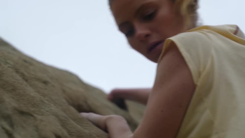Young blonde woman pushes herself up while climbing a rock wall on a mountain