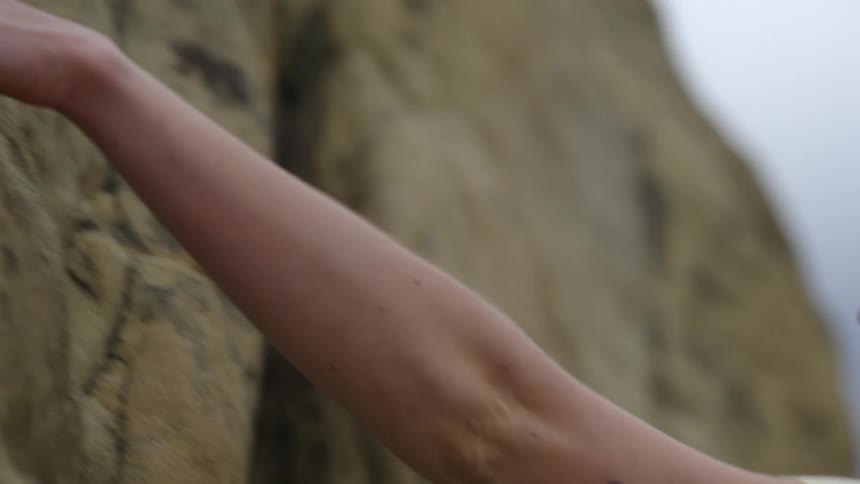 A woman climbs a rock face using her hands during the day