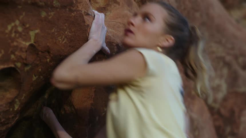 Young blonde woman pushes herself up while climbing a rock wall