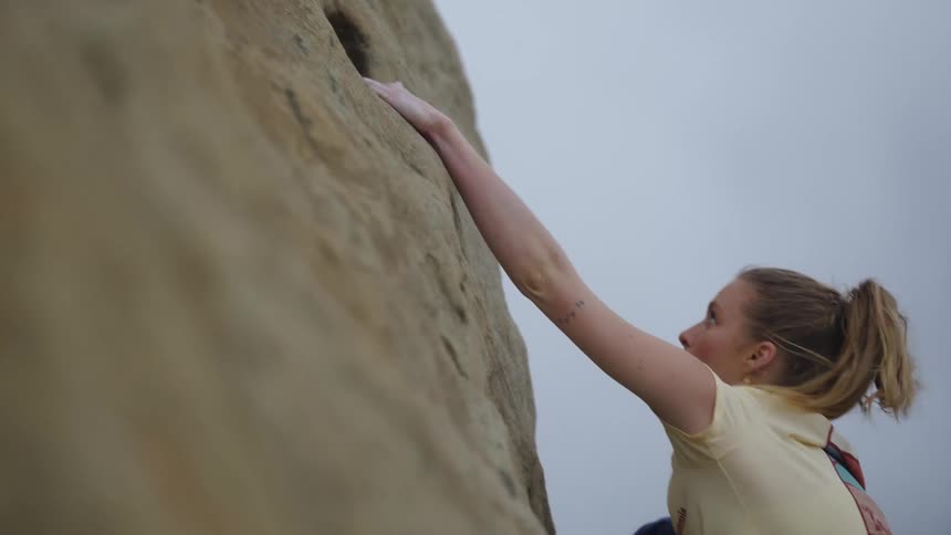A woman is climbing the side of a mountain and looks down as she pulls herself up