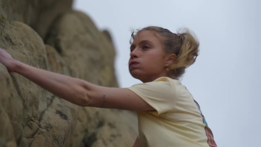 A woman is holding on to rocks and climbing the side of a mountain