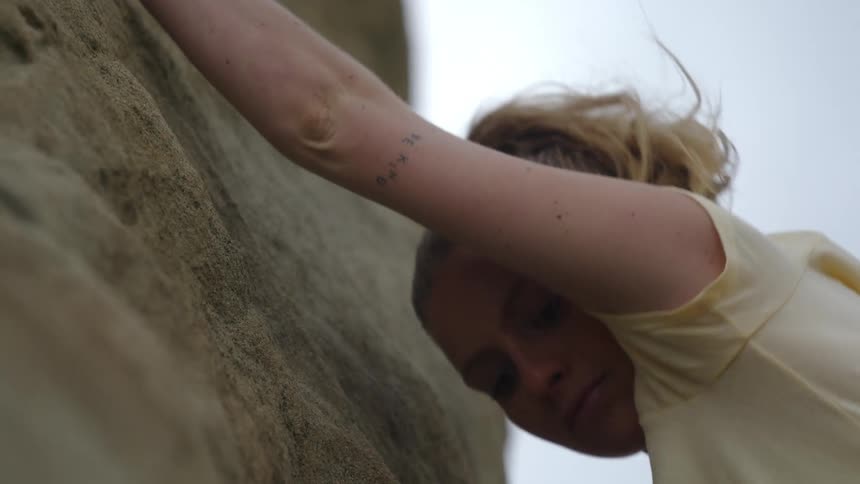A rock climber pulls herself up looking down to check her foothold