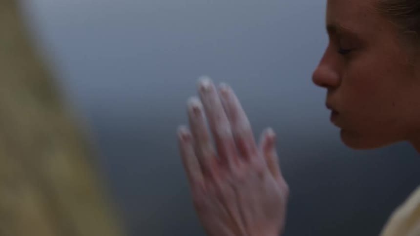 A rock climber chalks her hands and takes a deep breath before beginning to climb a rock face outdoors during the day