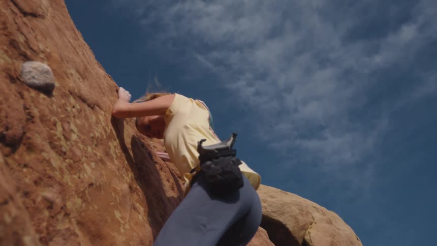 A determined woman carefully places her foot on a steep cliff while rock climbing