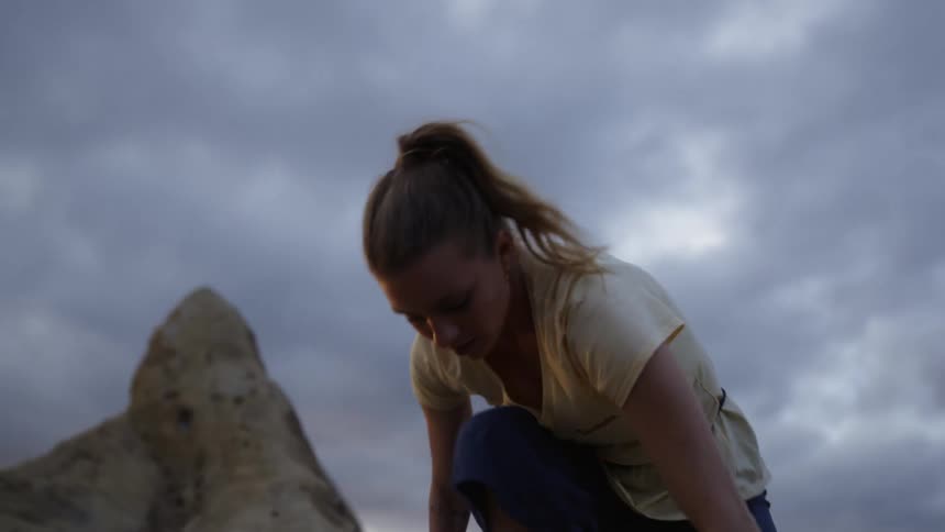 A woman climbs a rock face to reach the top of a cliff on a cloudy day