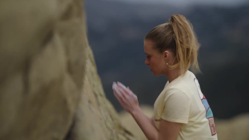 Young woman rubs her hand with white talcum before climbing a rock wall