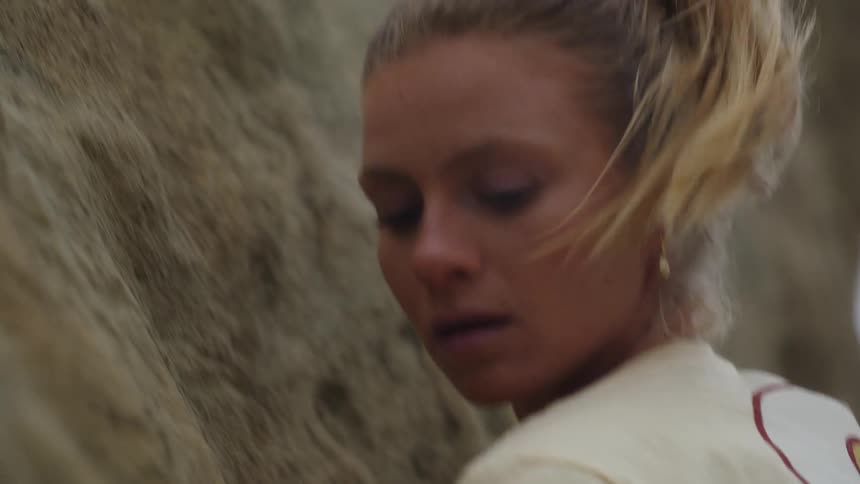 Young blonde woman pushes herself up while climbing a rock wall