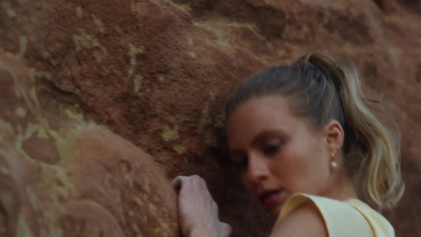 A woman is climbing the side of a mountain and holding on to rocks as she pulls herself up